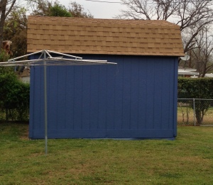 A 'cloud blue' storage shed with brown shingled roof. A rotary clothesline is in front and to the left of the shed. 